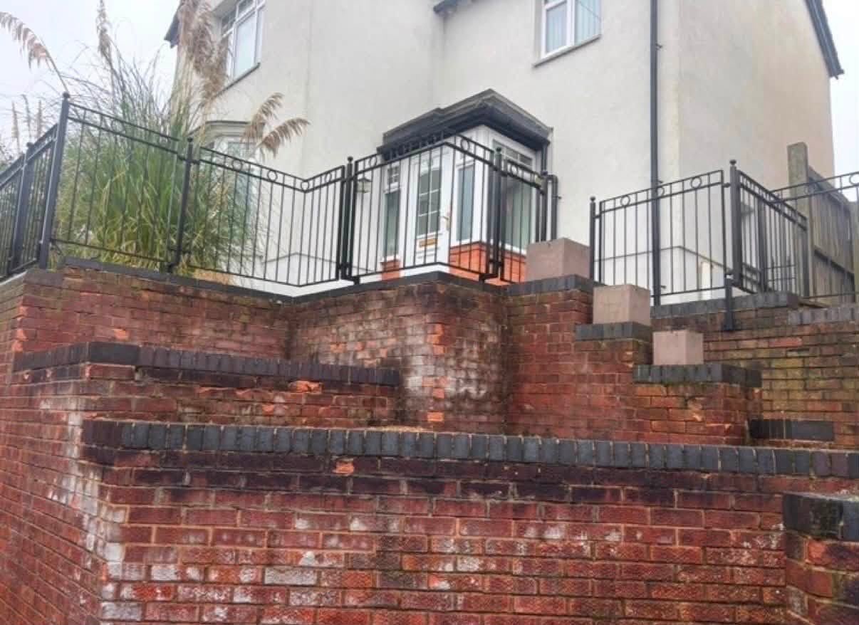 Before: the old retaining wall with weathered, stained brickwork and rusted railings in Northamptonshire